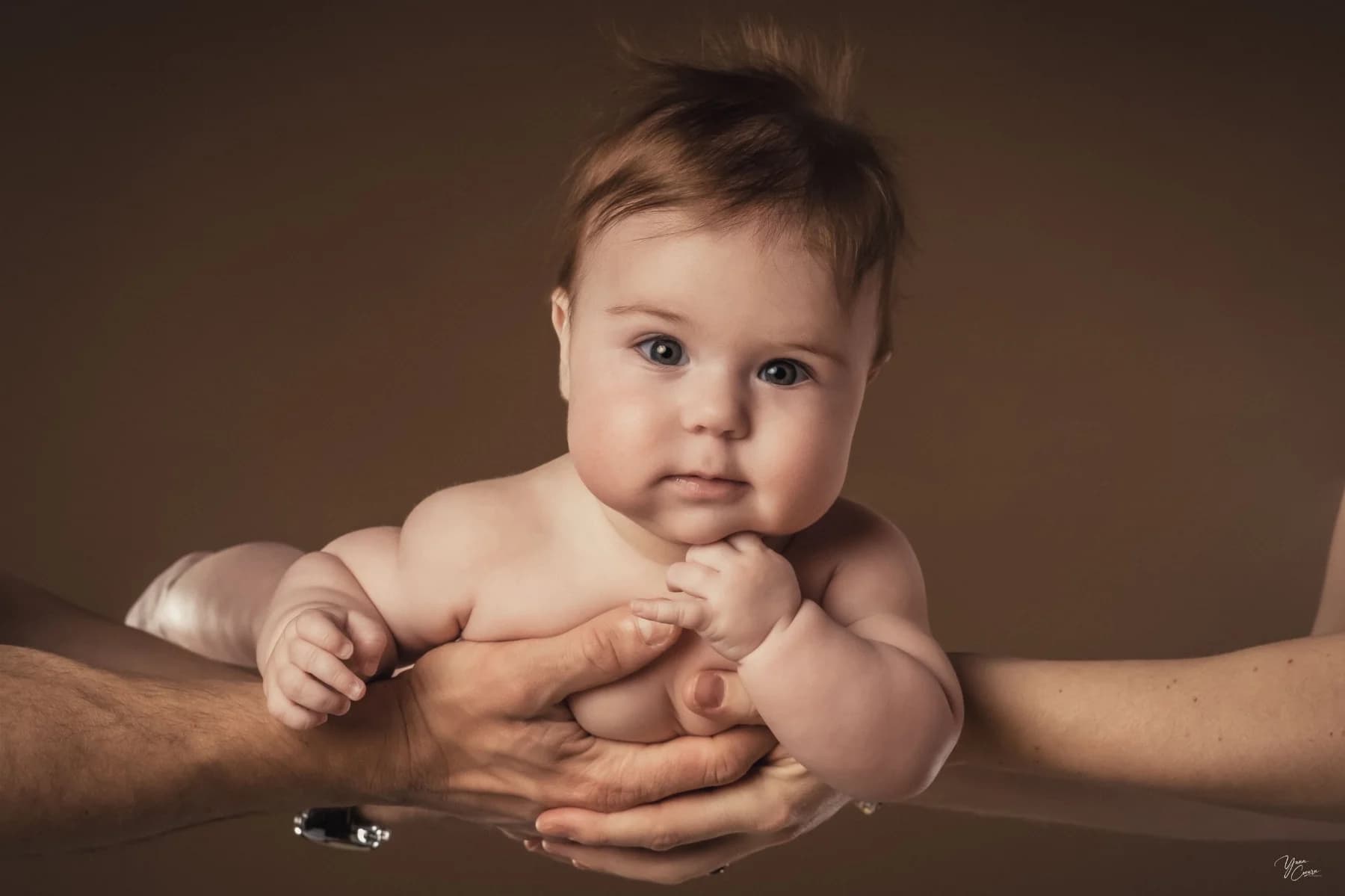 Bébé tenu dans les mains de ses parents en studio à Ruoms