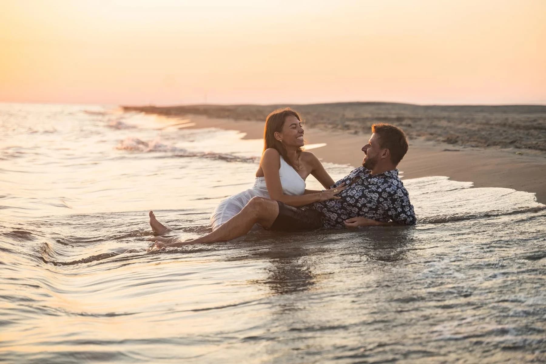 Couple assis dans l'eau au coucher de soleil rose sur la plage de l'Espiguette en Camargue