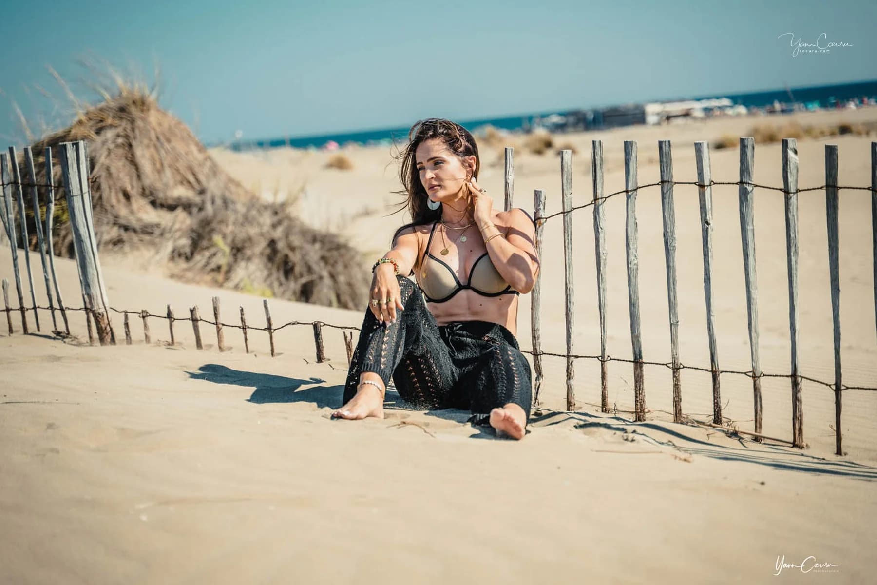 Femme assise contre les ganivelles, mer bleue en arrière-plan, Grau-du-Roi