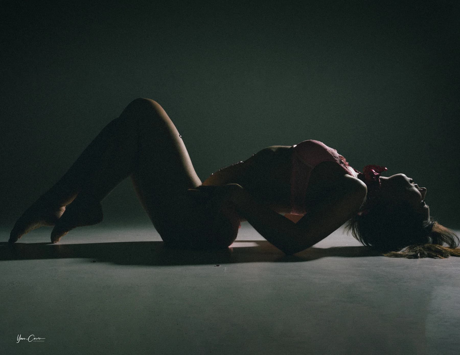 Femme en boudoir intime, pose sensuelle en studio avec éclairage dramatique et fond vert tendre