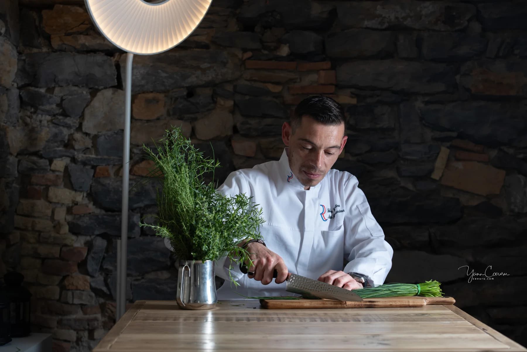 Chef restaurateur découpant des herbes sous une lumière tamisée, reportage d'entreprise en Ardèche.