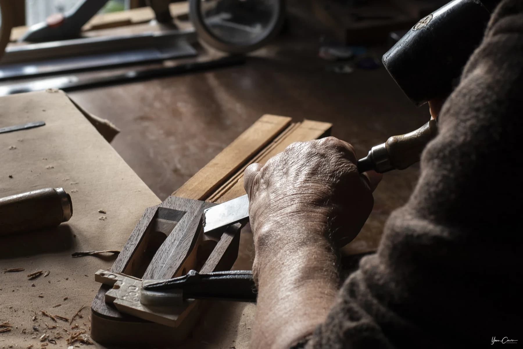 Artisan menuisier au travail dans son atelier, Entreprise à Saint Genest de Bauzon, mains expertes sur ciseau à bois.