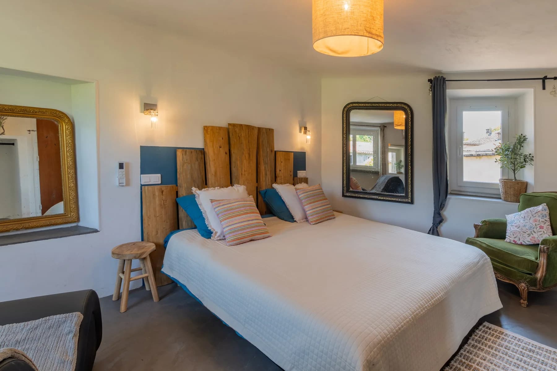 Immobilier Vaucluse : chambre lumineuse avec tête de lit en bois brut et coussins bleus, ambiance chaleureuse et authentique.