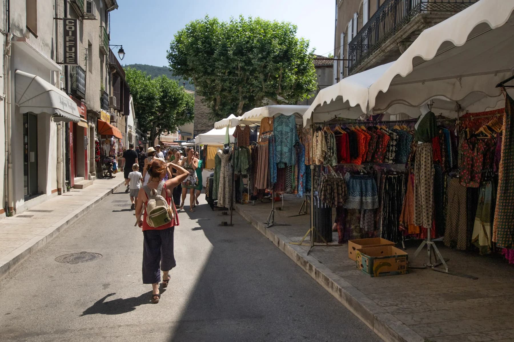 Immobilier Vaucluse, marché provençal animé avec stands de vêtements colorés sous le soleil d'été.