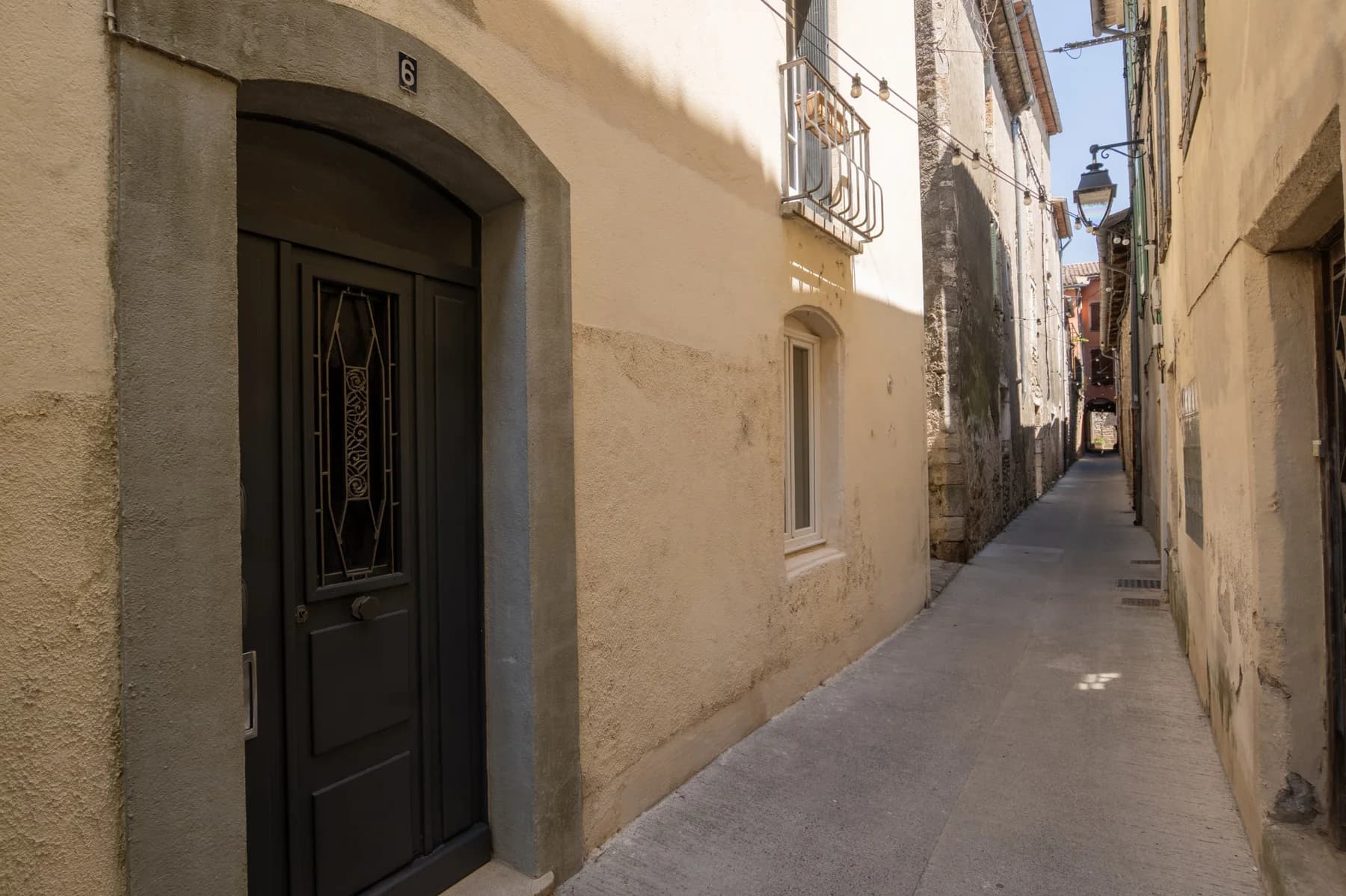 Immobilier Vaucluse, ruelle étroite en pierre avec porte ancienne numéro 6 et balcon, ambiance village provençal.