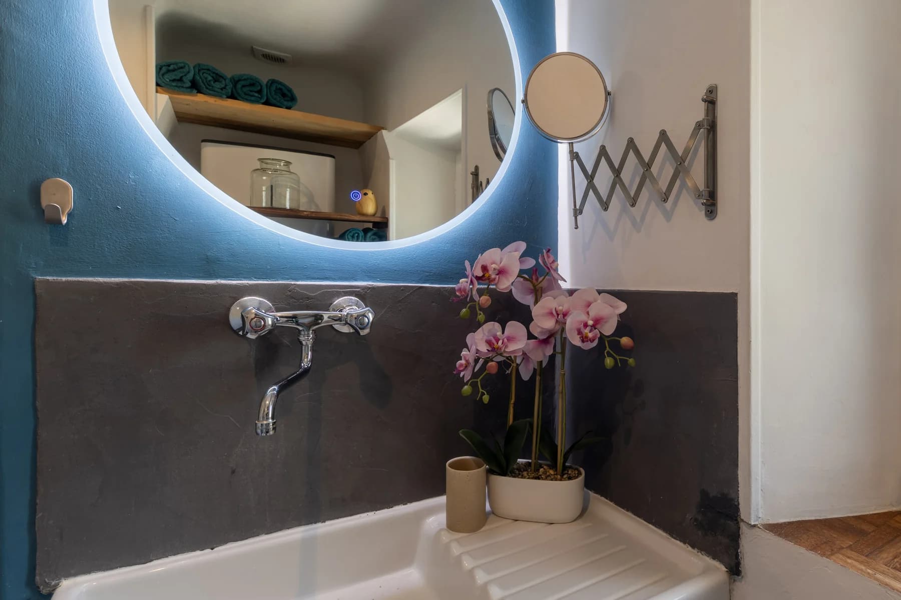 Immobilier Vaucluse – salle de bain design avec miroir LED rond, robinet mural chromé et orchidée rose en décoration.
