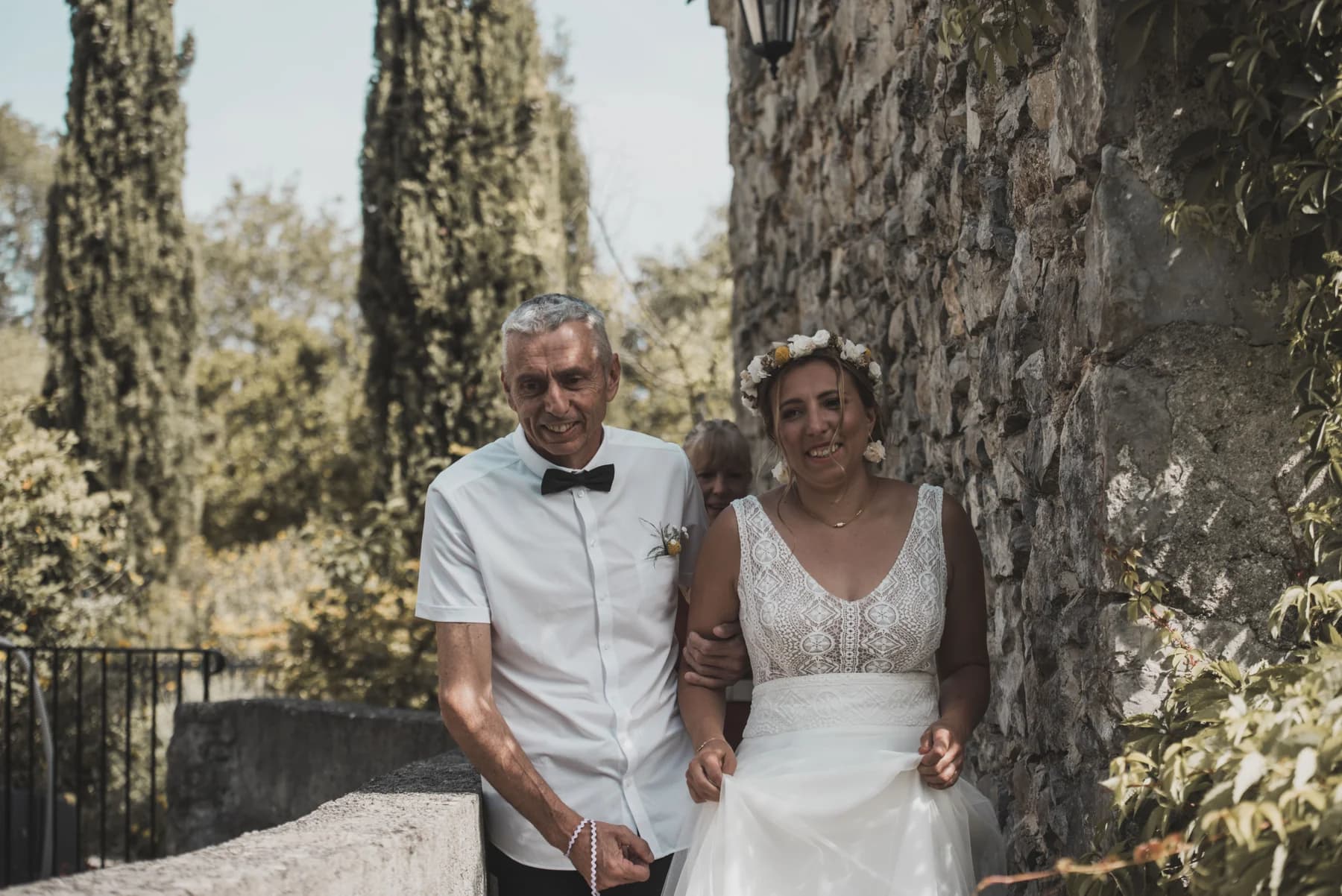La mariée et son père devant un mur de pierre et des cyprès — Domaine de Bagard, Sauve (Gard)