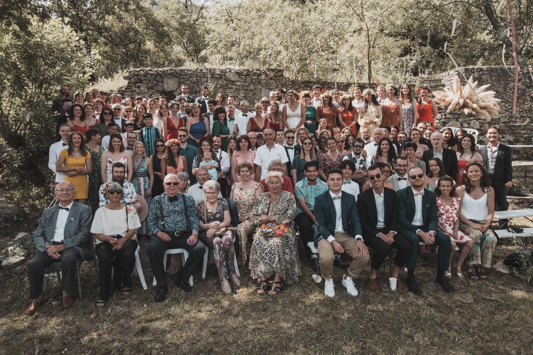Photo de groupe des invités devant le mur de pierre — mariage au Domaine de Bagard, Sauve
