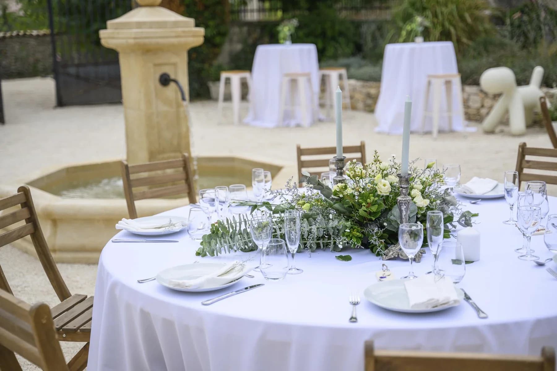 Mariage au Domaine de la Bedosse, à Alès : table ronde décorée fleurs blanches, vaisselle élégante et fontaine en pierre