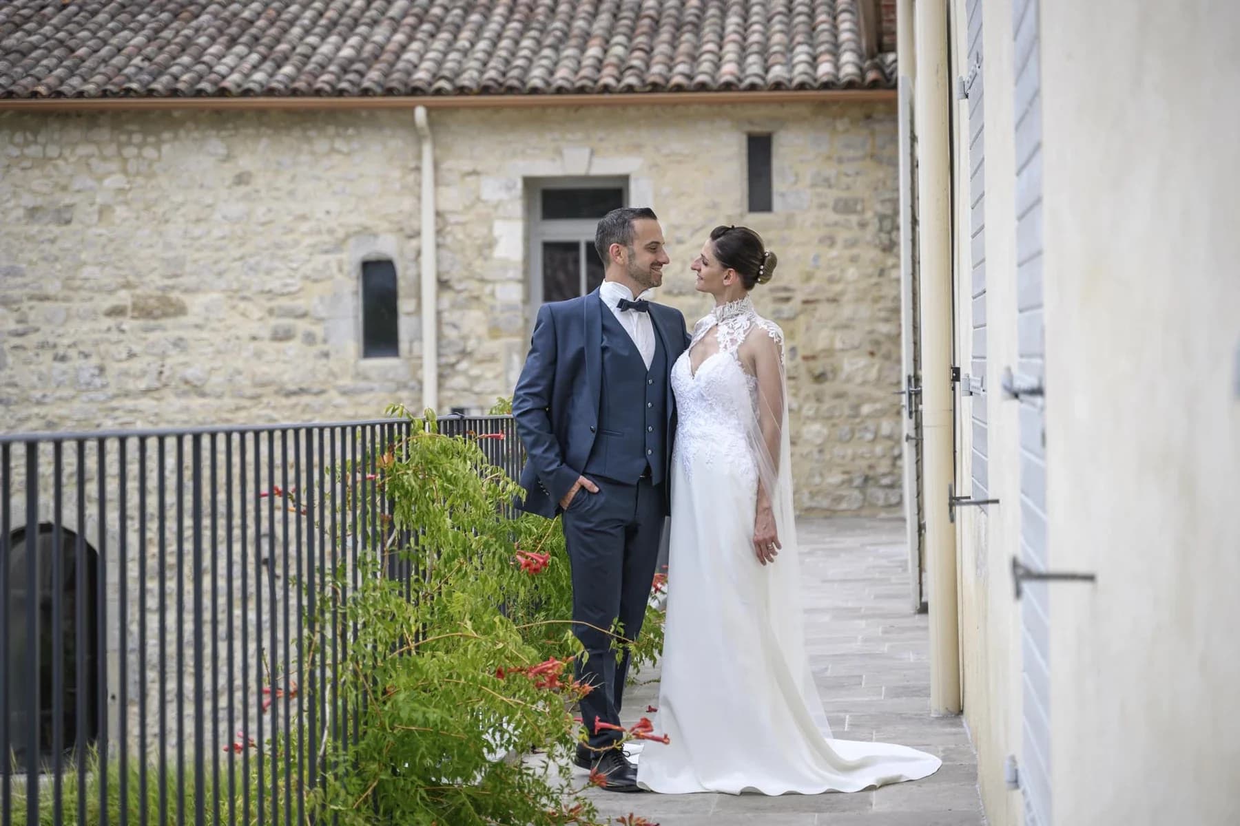 Couple de mariés en costume et robe blanche devant ancienne maison en pierre, mariage en Ardèche