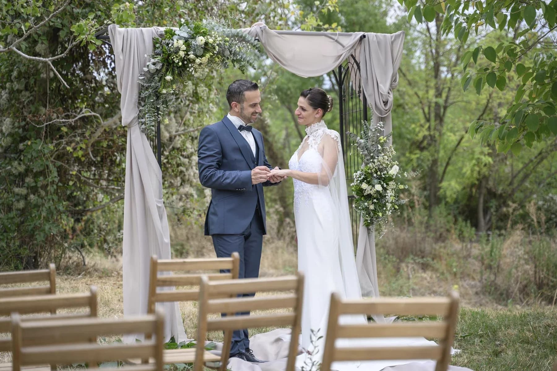 Mariage au Domaine de la Bedosse, à Alès, échange des alliances sous arche fleurie en pleine nature verdoyante