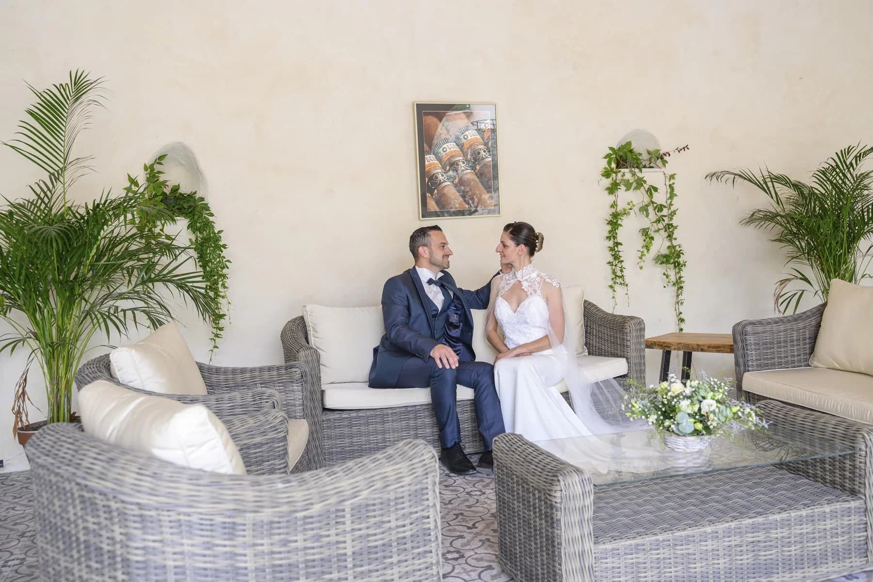 Mariés dans un salon élégant au Domaine de la Bedosse, à Alès, couple souriant assis sur canapé gris, décoration florale et plantes vertes