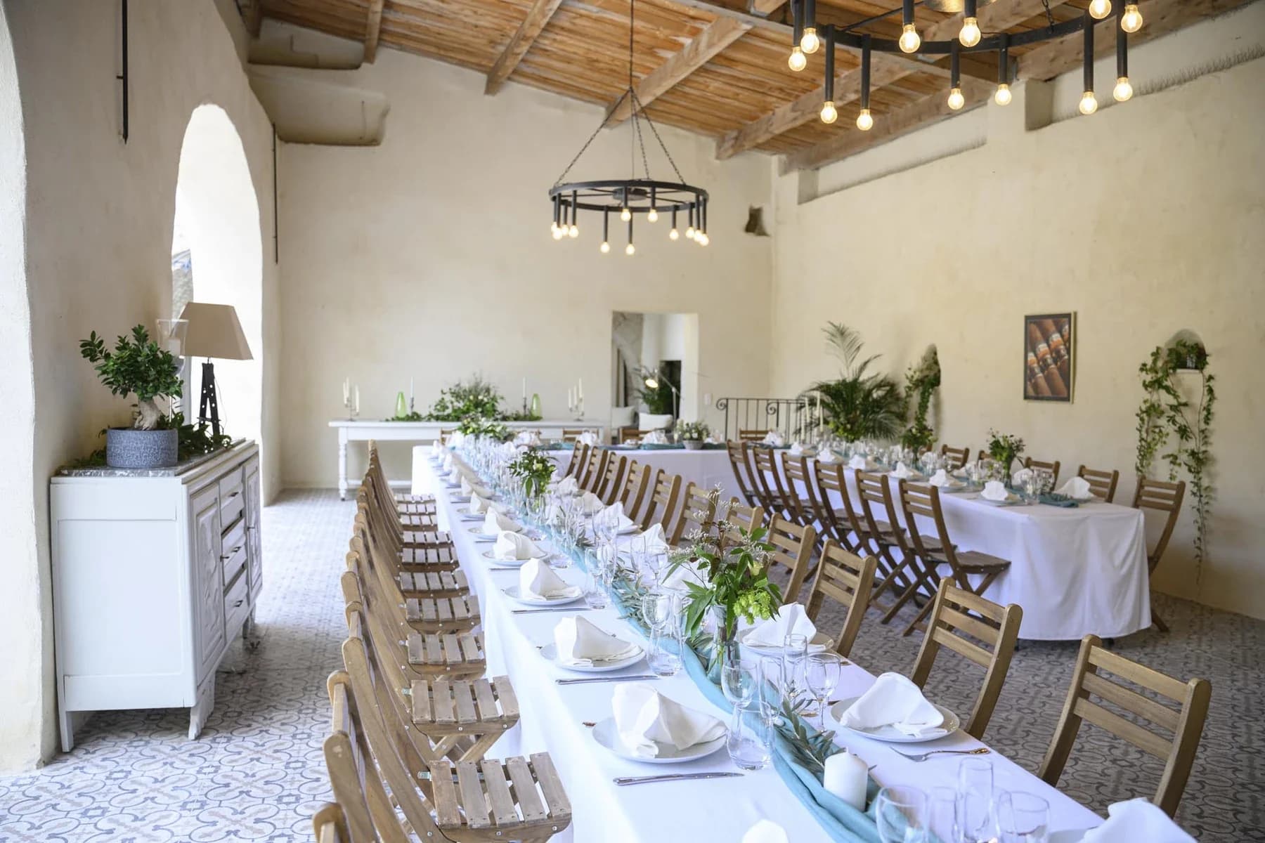 Salle de réception élégante pour mariage en Ardèche avec tables blanches, chaises en bois et décoration florale minimaliste