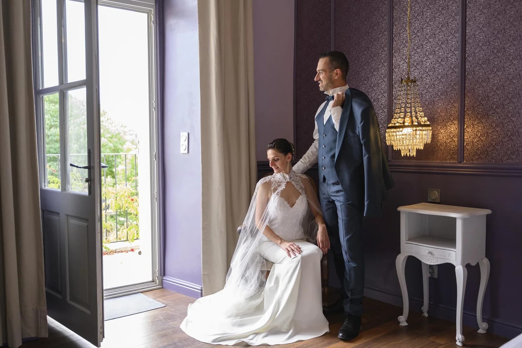 Couple élégant en tenue de mariage dans un salon avec lustre dorée, mariage en Ardèche sophistiqué