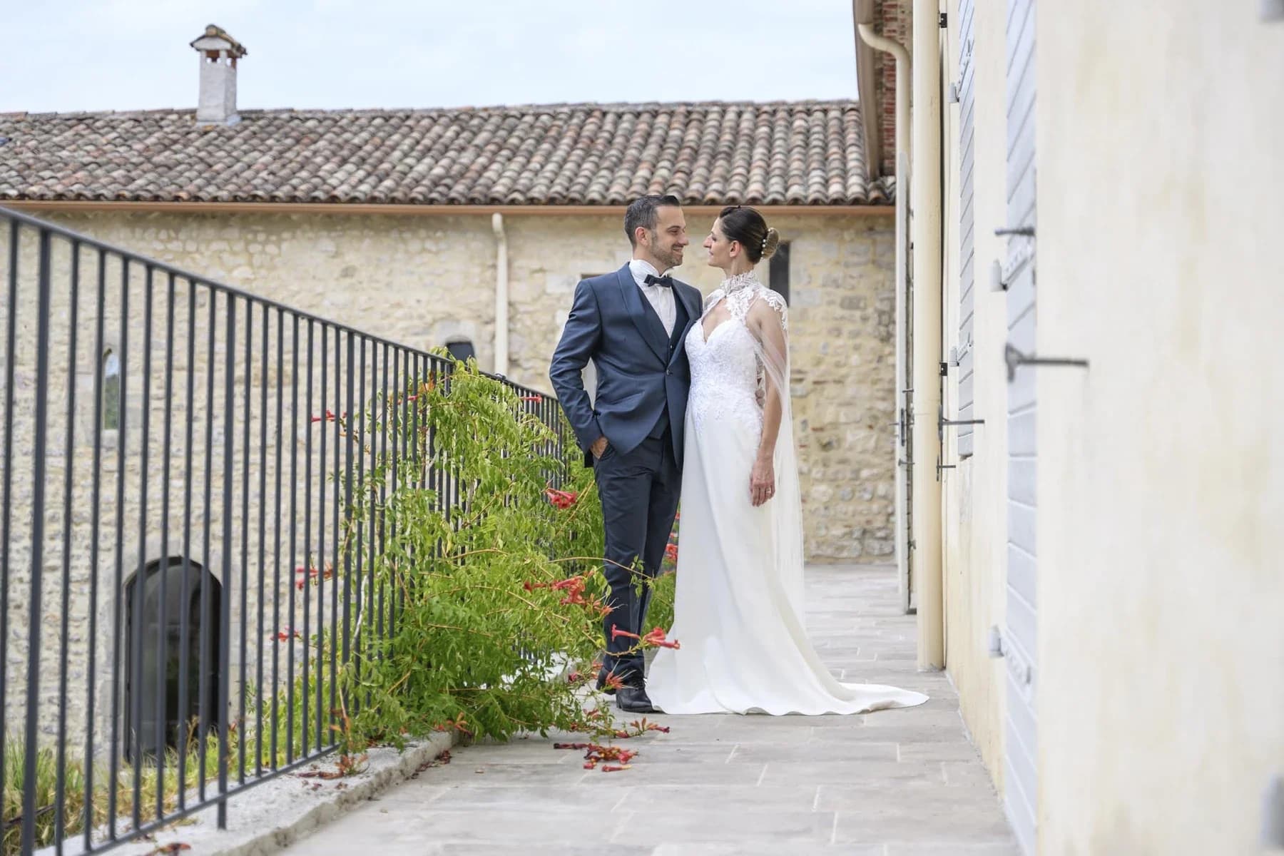 Couple de mariés souriants sur terrasse de pierre au Domaine de la Bedosse, à Alès, robe blanche et costume bleu marine, ambiance lumineuse