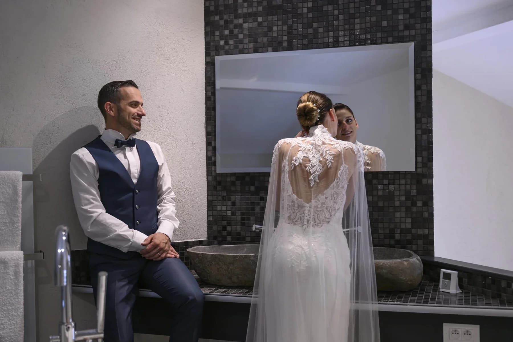 Couple de mariage dans salle de bain moderne au Domaine de la Bedosse, à Alès, mariée en robe dentelle face au miroir, marié en costume bleu