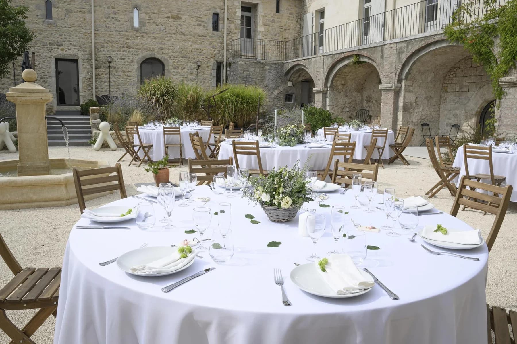 Mariage au Domaine de la Bedosse, à Alès : réception en cour intérieure avec tables rondes dressées, décoration florale élégante et architecture en pierre