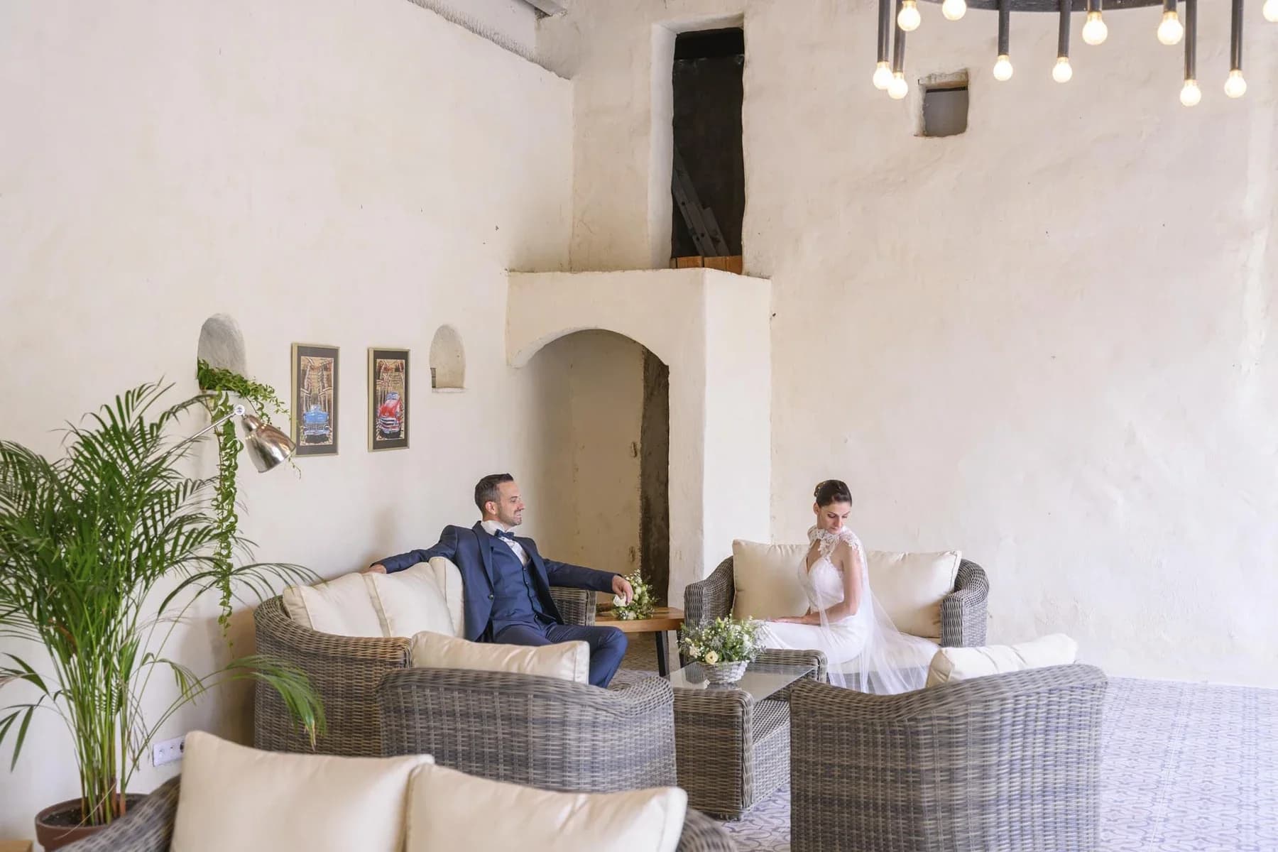 Couple de mariés assis dans un salon blanc minimaliste, mariage au Domaine de la Bedosse, à Alès, lumière naturelle douce, ambiance élégante et intime