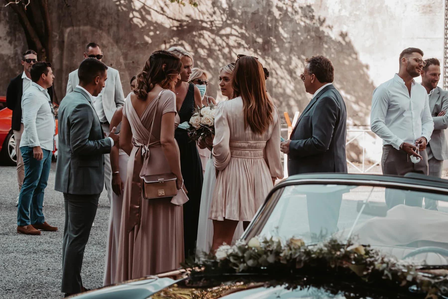 Mariages à Aubenas, invités élégants échangeant autour d'un bouquet de roses blanches près d'une voiture de collection.