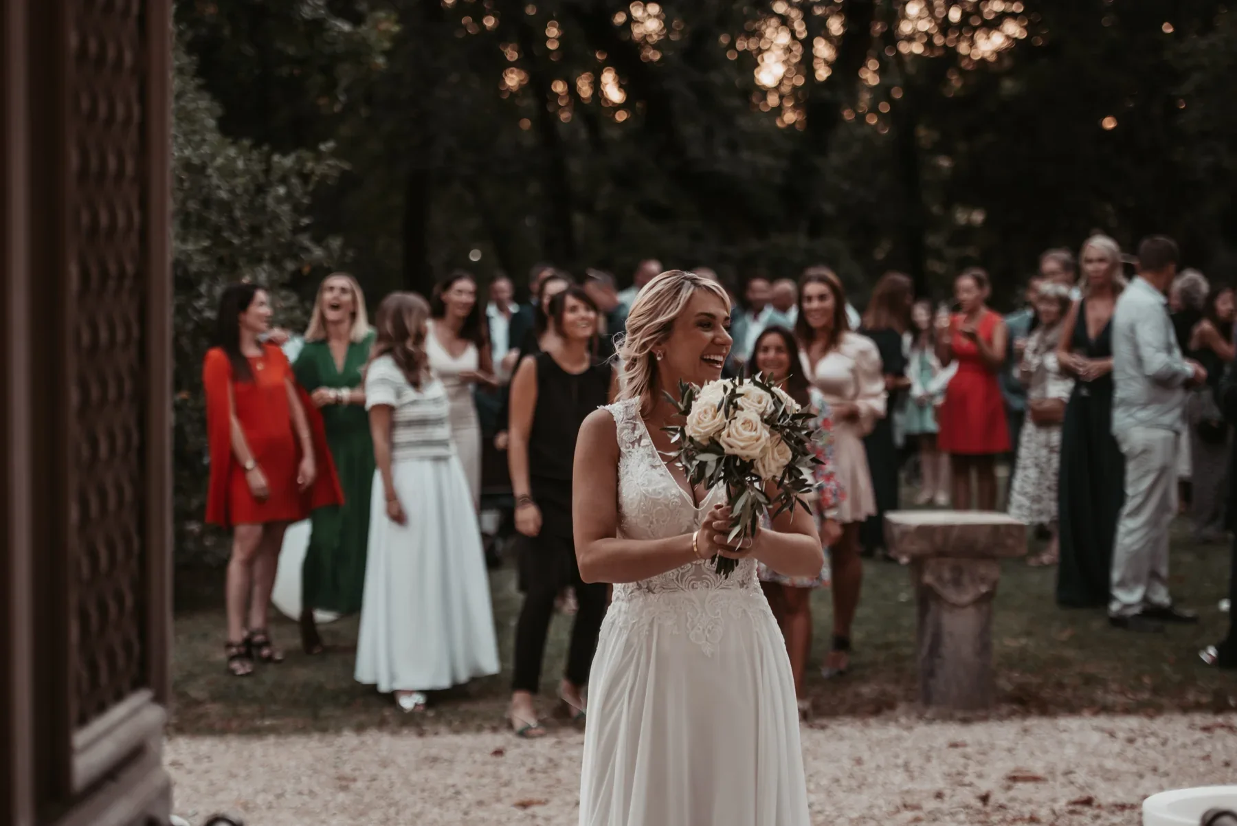 Mariée souriante tenant un bouquet de roses blanches entourée de ses invités lors d'un Mariage à Aubenas.