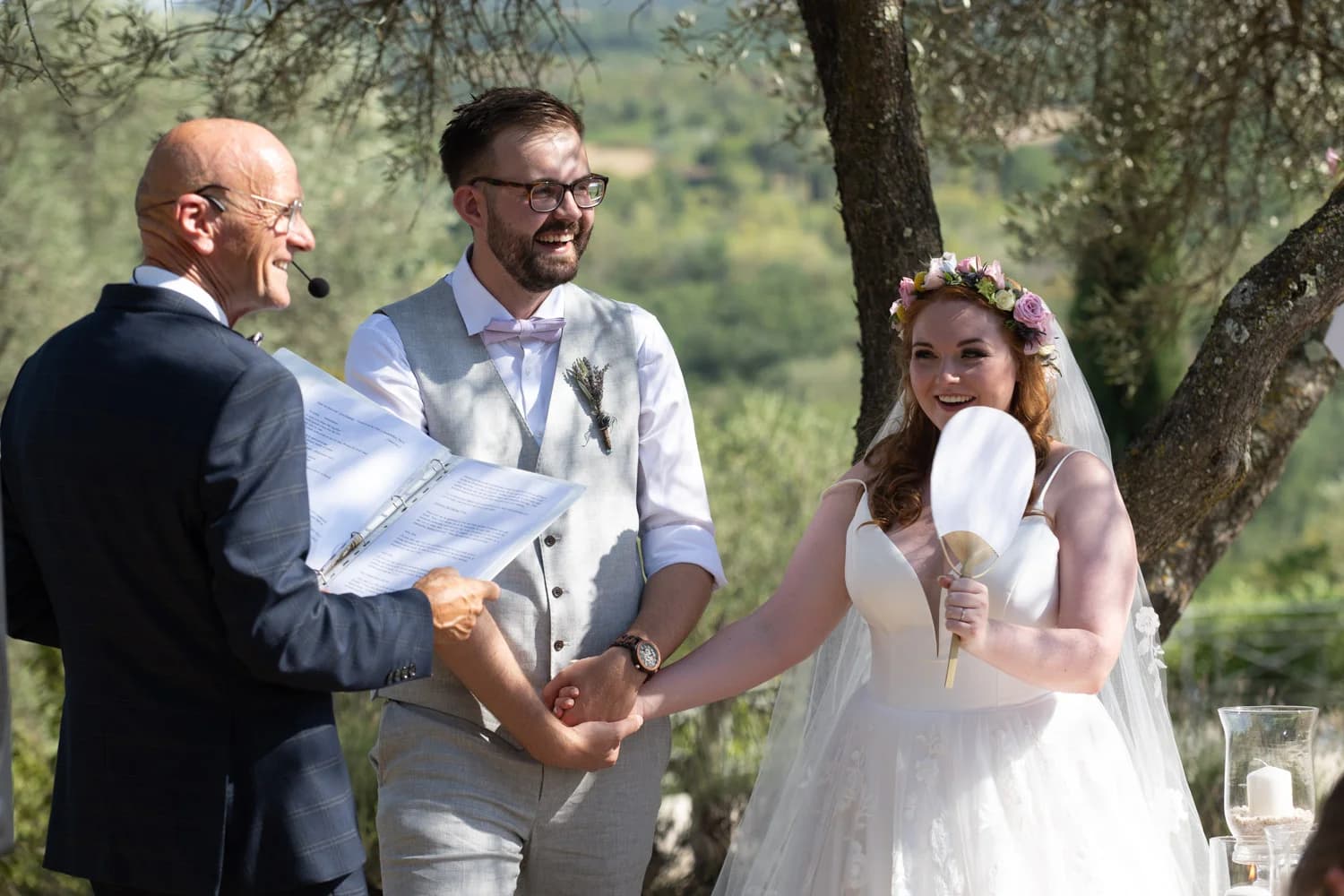 Mariages en plein air, couple souriant échangeant ses vœux avec officiant, mariée couronnée de fleurs.