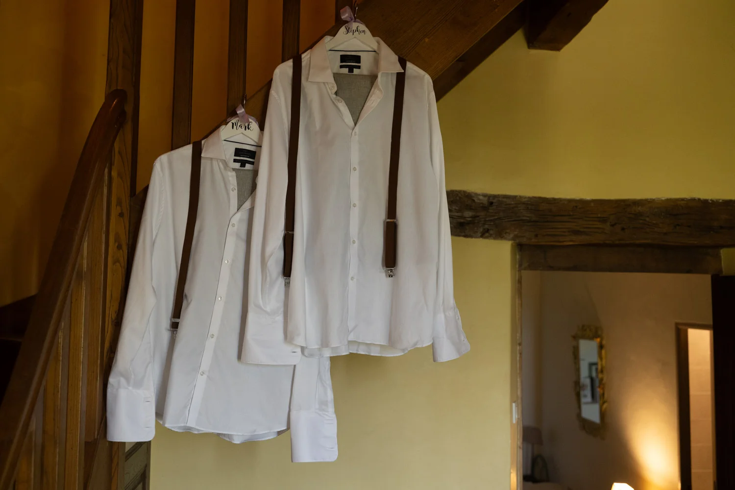 Mariages au Clos d'Hullias : chemises blanches et bretelles marron sur cintres personnalisés, ambiance champêtre.
