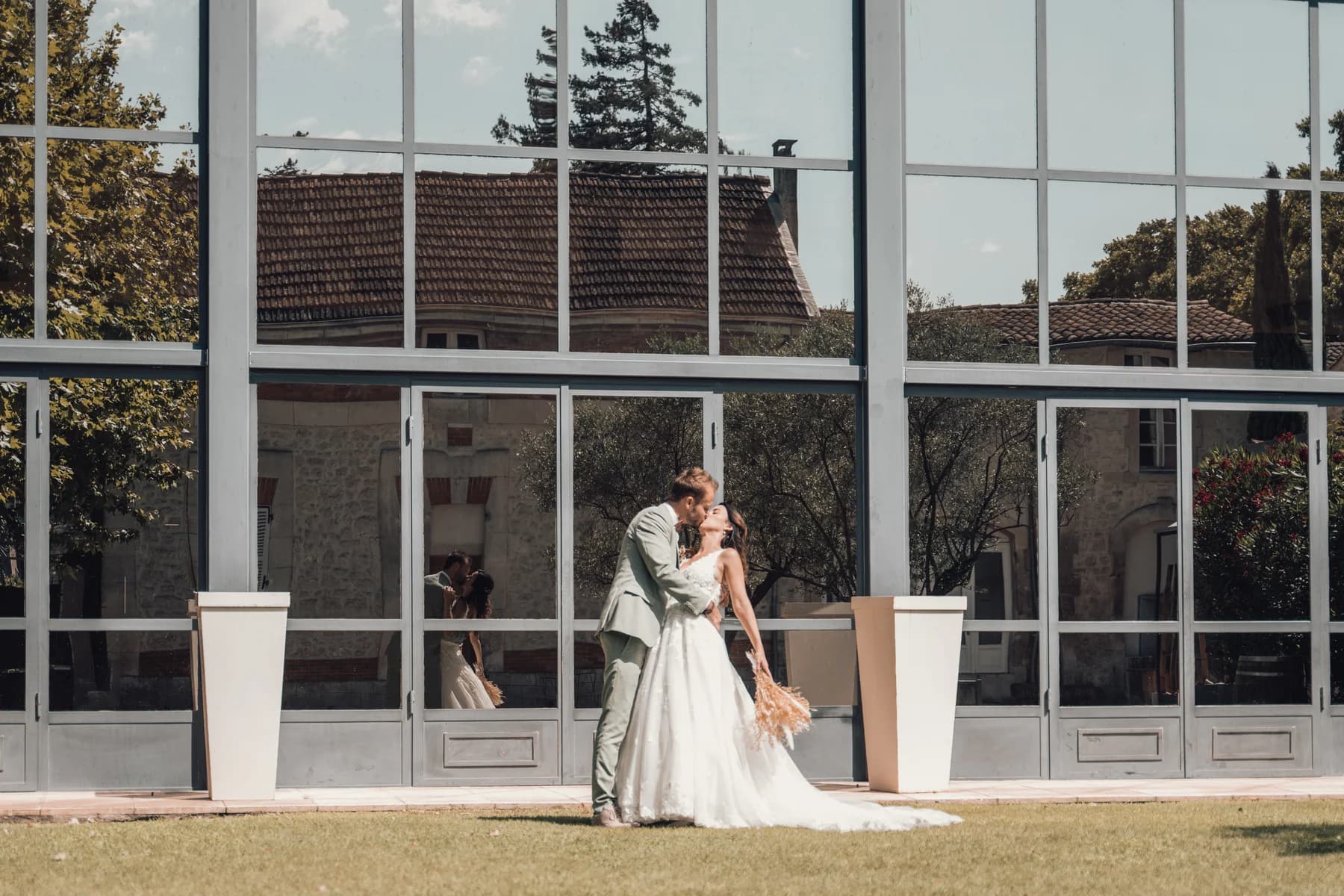 Mariages au domaine du trusquin Pierrelatte Drôme, couple s'embrassant devant une grande verrière lumineuse.