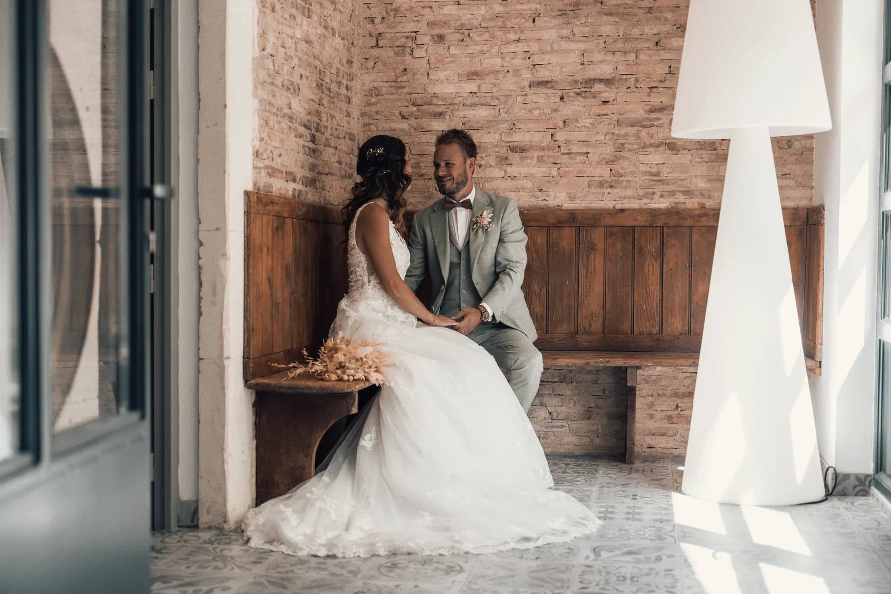 Mariages au domaine du trusquin Pierrelatte Drôme, couple assis sur un banc en bois face à un mur de briques, ambiance intime.