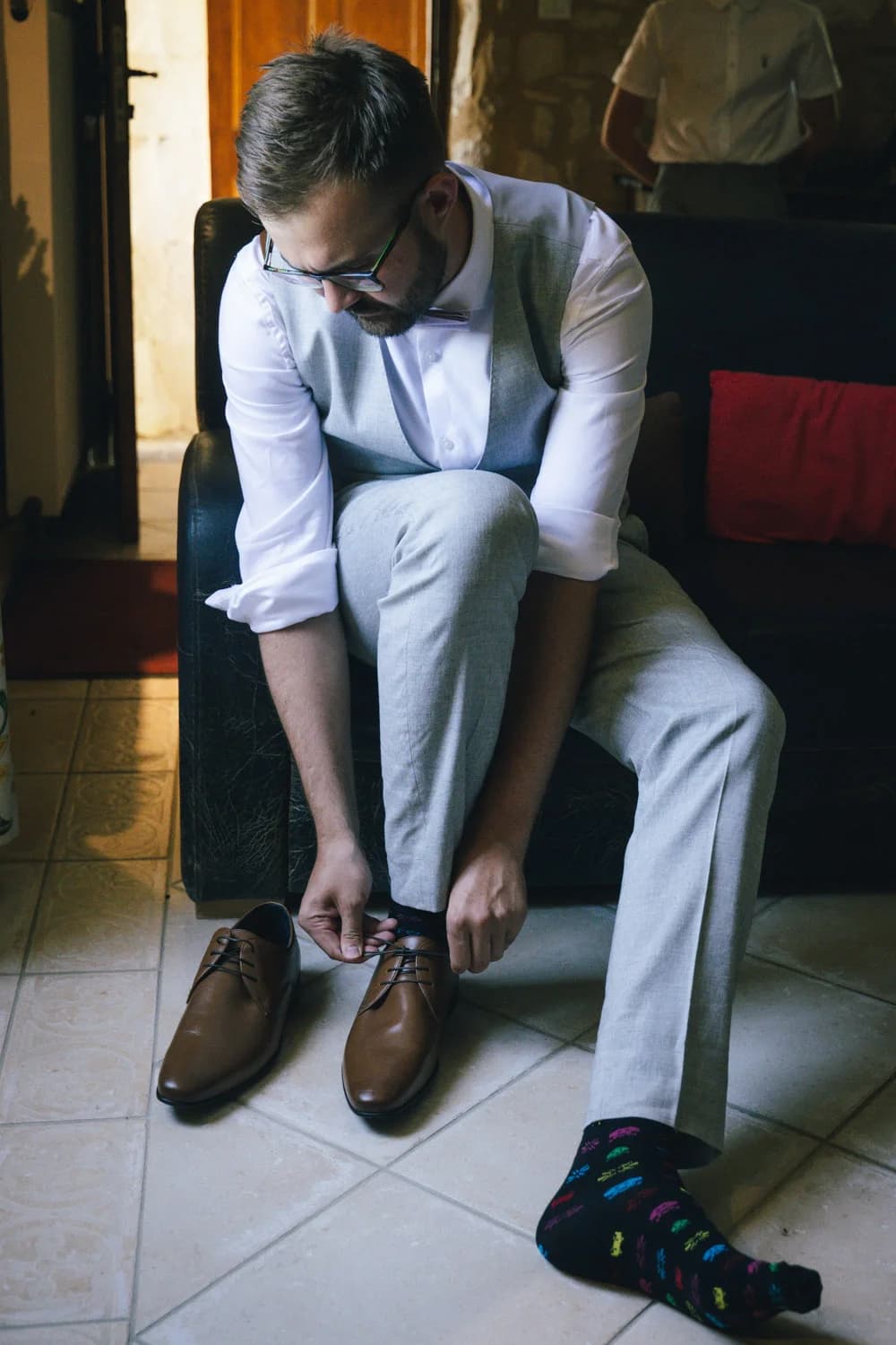 Mariages : marié en costume gris et chaussettes colorées qui lace ses chaussures marron avant la cérémonie.