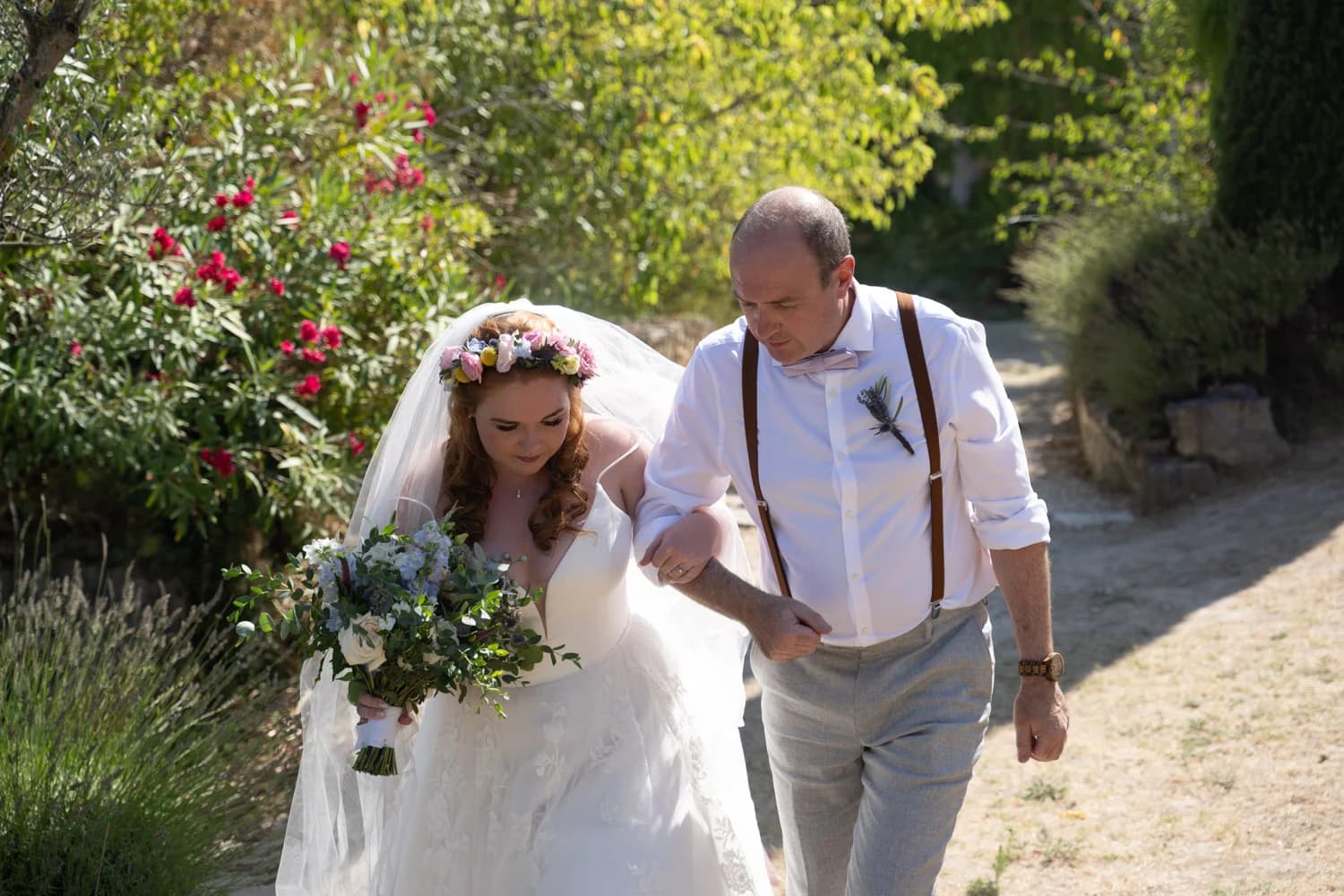 Mariages en plein air, mariée en robe blanche avec couronne florale et bouquet, accompagnée dans un jardin verdoyant.