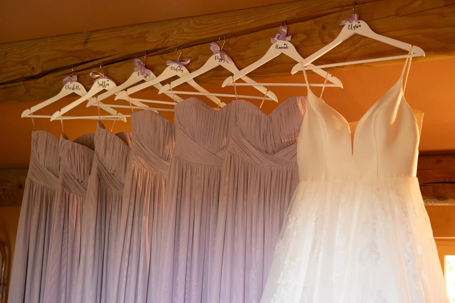 Mariages : robes de demoiselles d'honneur lilas et robe de mariée blanche sur cintres personnalisés.