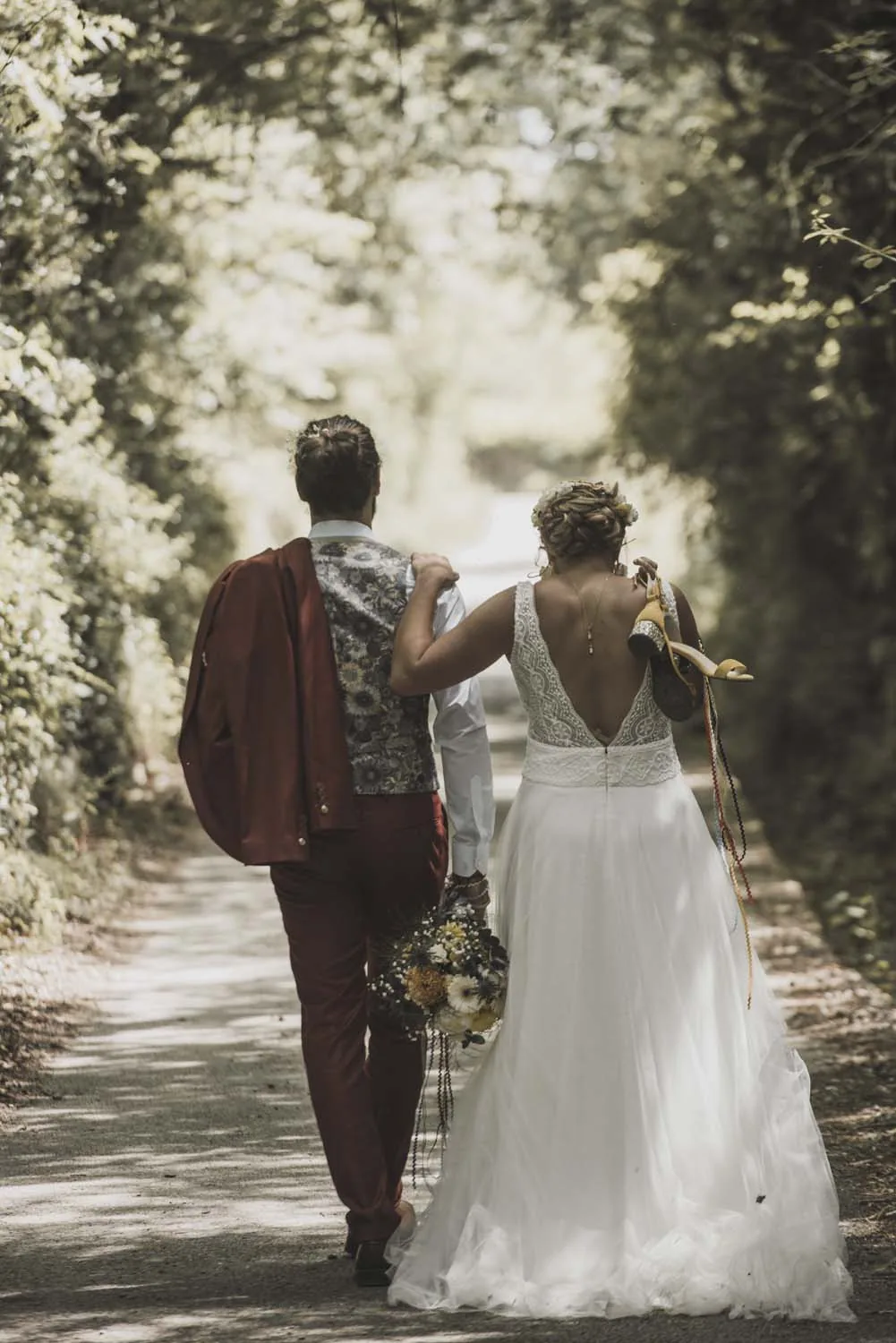 Couple de mariés marchant de dos sur un chemin bordé d'arbres en Ardèche